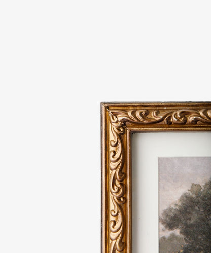 Gold ornate frame with a painting of trees on a white background